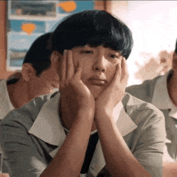 a young man with his hands on his face is sitting in a classroom with other students