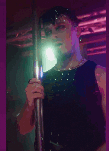 a man in a black tank top is standing on a pole in a dark room