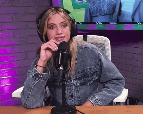 a woman in a denim jacket is sitting in front of a microphone