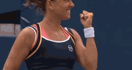 a woman in a black tank top is holding her fist in the air and smiling .