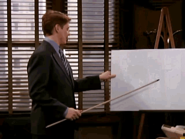 a man in a suit and tie is pointing at a whiteboard