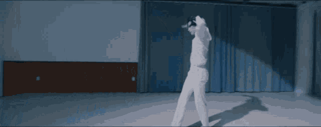 a man in a white shirt and white pants is dancing in a dark room