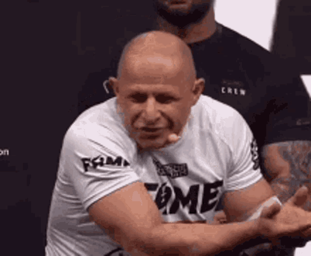 a bald man wearing a white shirt with the word fame on it .