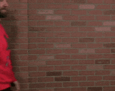 a man with a beard is wearing a red sweater with a godzilla on it and a beanie .