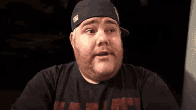 a man with a beard wearing a hat and a black shirt with the word miami on it