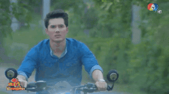 a man in a blue shirt is riding a motorcycle down a dirt road