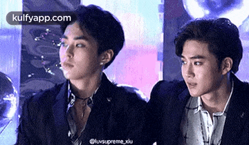 two young men in suits are standing next to each other and looking at the camera .