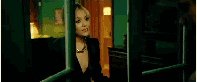 a woman in a black suit and gold necklace is standing in a doorway .