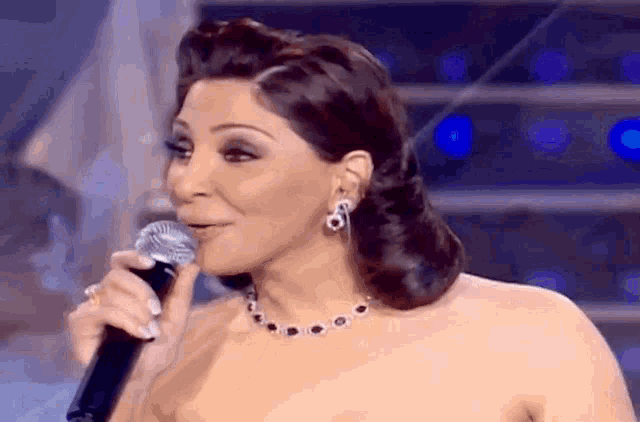 a woman is singing into a microphone while wearing a necklace