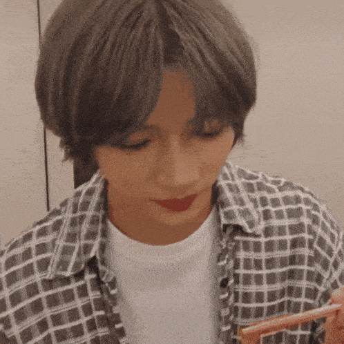 a woman wearing a plaid shirt and red lipstick is eating something with chopsticks .