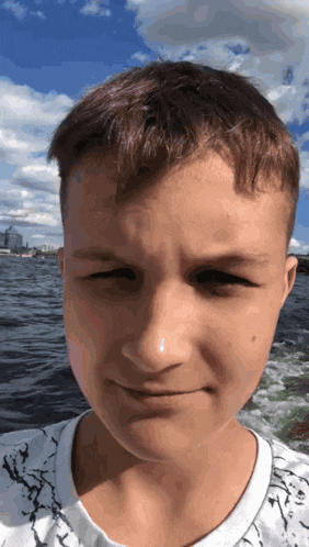 a close up of a young boy 's face with a boat in the background