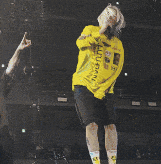 a woman singing into a microphone wearing a yellow shirt that says lulu dan on it