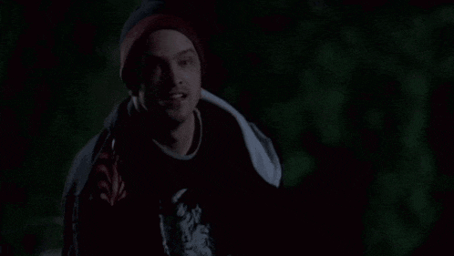 a man wearing a beanie and a red shirt is smiling in the dark .