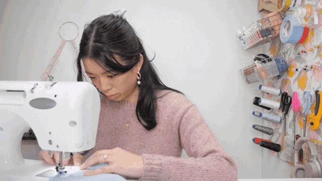 a woman wearing a pink sweater is using a sewing machine