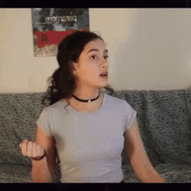 a woman is sitting on a couch in front of a wall with a poster that says " enigma "