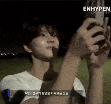 a person is taking a picture with a cell phone and the word enhypen is on the bottom