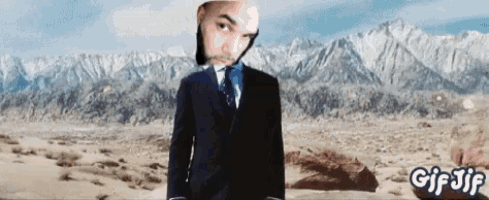 a man in a suit and tie stands in the desert with mountains in the background and the words gif jif below him