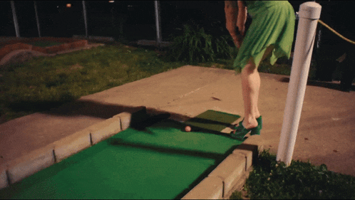 a woman in a green dress is playing miniature golf