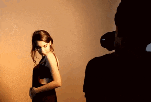 a woman in a dress is being photographed by a man in a dark room .