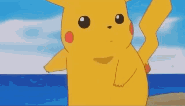 a close up of a cartoon pikachu standing on a beach near the ocean .