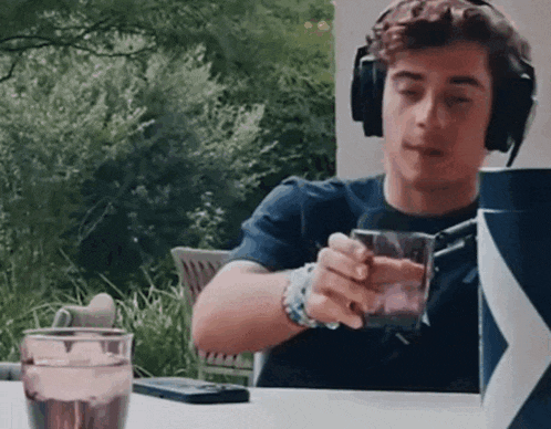 a man wearing headphones is sitting at a table with a glass of water and a cell phone .