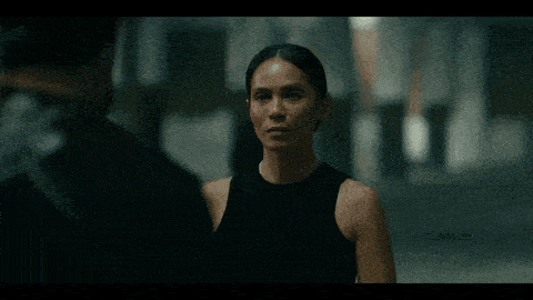 a woman in a black tank top is talking to a man in a black shirt in a movie .