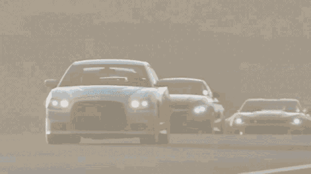 a white car is driving down a foggy road with other cars
