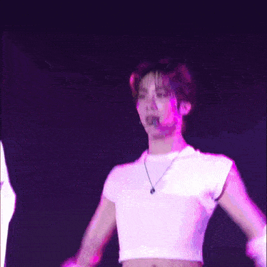 a man in a white crop top is dancing on a stage with his arms outstretched .