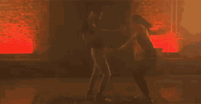 a couple of people are dancing in a dark room with red lights behind them .