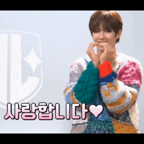 a young man wearing a colorful sweater is making a heart shape with his hands .