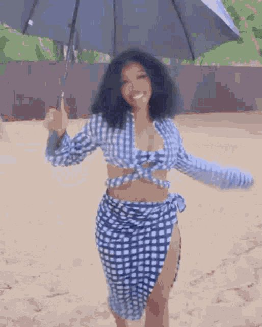 a woman in a blue and white plaid shirt and skirt is holding an umbrella on the beach .