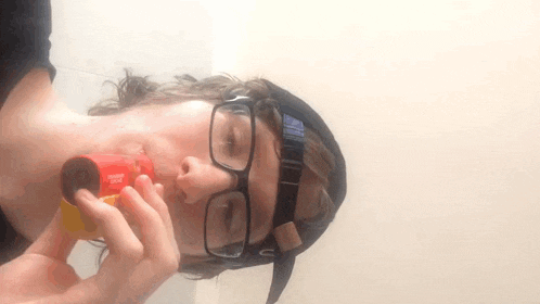 a man wearing glasses and a hat is holding a container that says snickers in his mouth