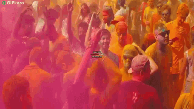 a man in a yellow hat is dancing in front of a pink background with a gifkaro logo in the corner .