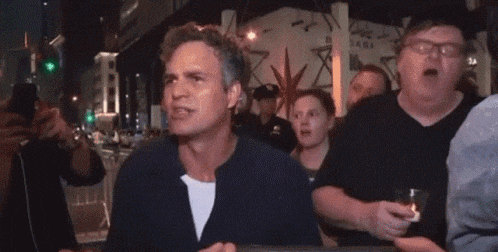 a man in a blue shirt is standing in a crowd of people holding a glass .