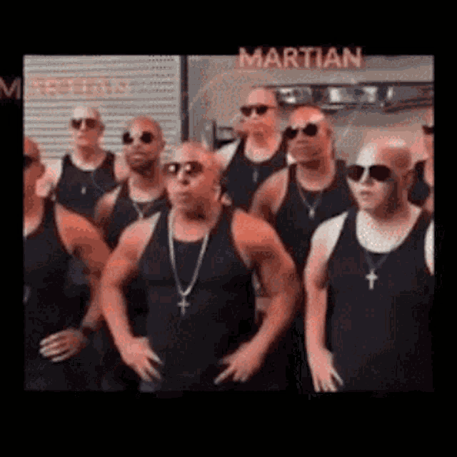 a group of men in black tank tops and sunglasses are standing in front of a martian sign .