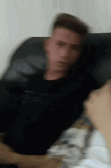 a blurry picture of a man in a black shirt sitting on a couch .