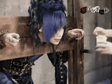 a person with blue hair is tied to a wooden plank