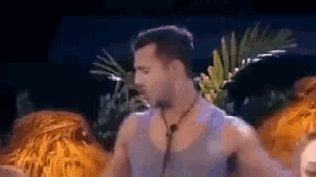 a man in a tank top is dancing in front of a palm tree at night .