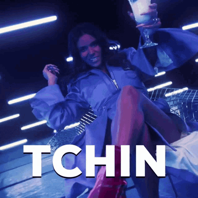 a woman in a purple coat is holding a glass with the word tchin written on it