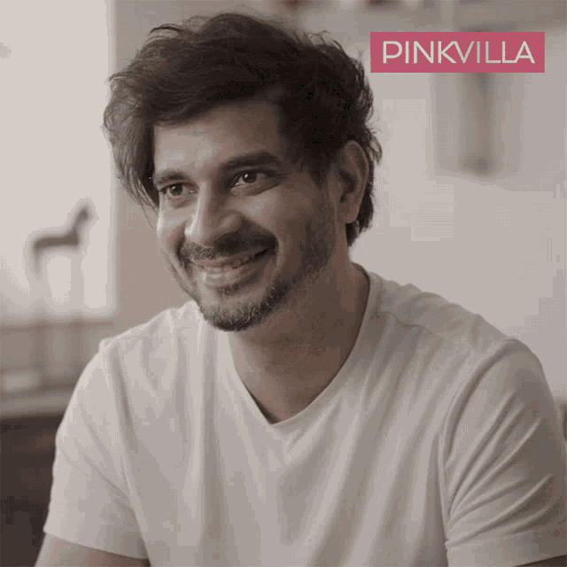 a man in a white t-shirt is smiling in front of a pink villa banner