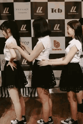 three girls standing in front of a wall that says ll tob