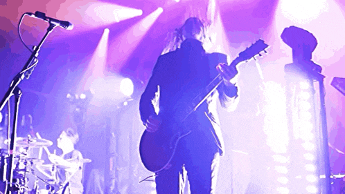 a man playing a guitar in front of a purple light