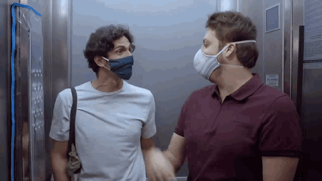 two men wearing face masks are in an elevator