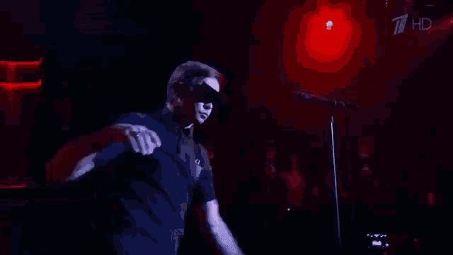 a man wearing a blindfold singing into a microphone in front of a 7 hd sign