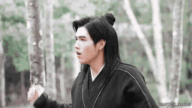 a man with long hair is standing in a forest .
