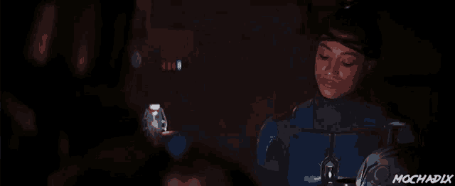 a woman in a blue suit is standing in a dark room next to a vase with the word mochadix on the bottom right