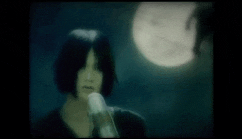 a woman is standing in front of a full moon in the dark .