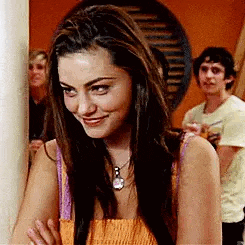 a woman is leaning against a wall and smiling while a man stands behind her .