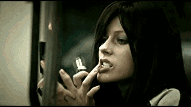 a woman is applying lipstick while smoking a cigarette in front of a mirror .