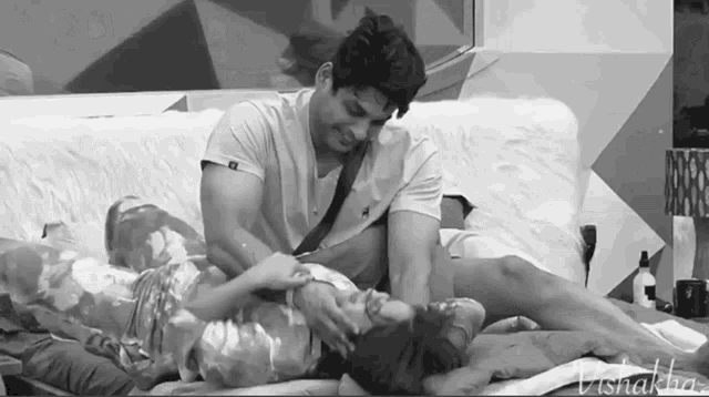 a black and white photo of a man and woman laying on a couch with the name vishakha on the bottom right